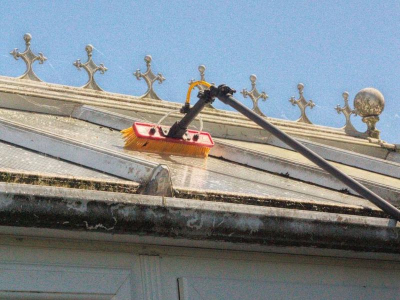 A water-fed pole brush cleaning a conservatory roof beside a gutter