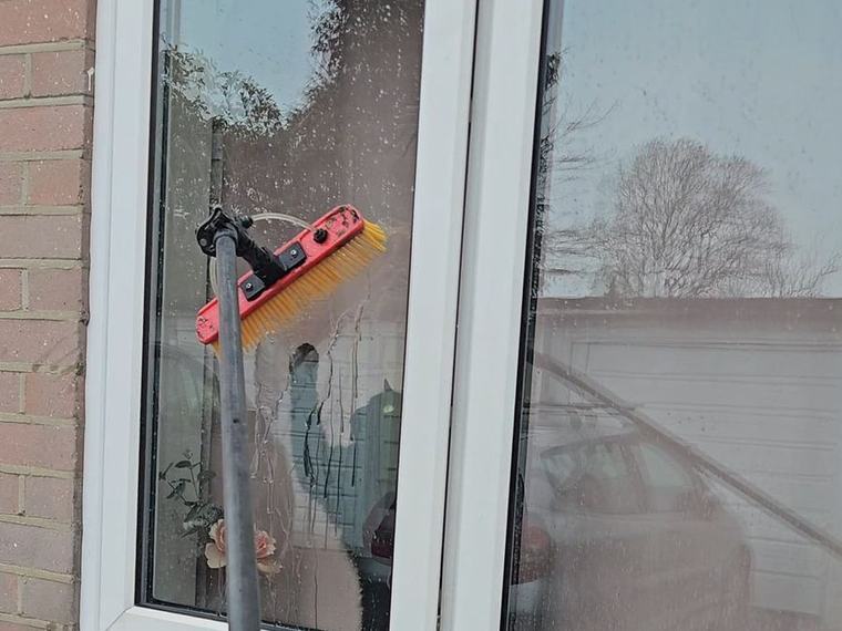 A water-fed pole brush cleaning a white UPVC window